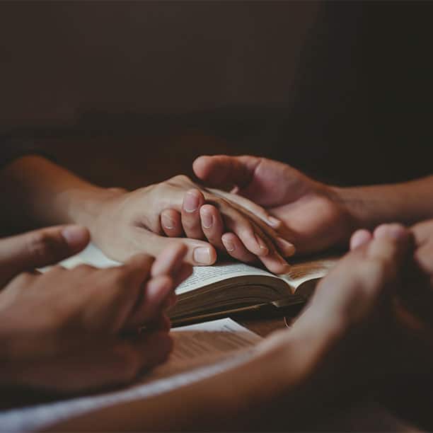 Group Of People Holding Hands On Bible Praying