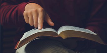 Person Wearing Red Sweeter Pointing On Glossary Book